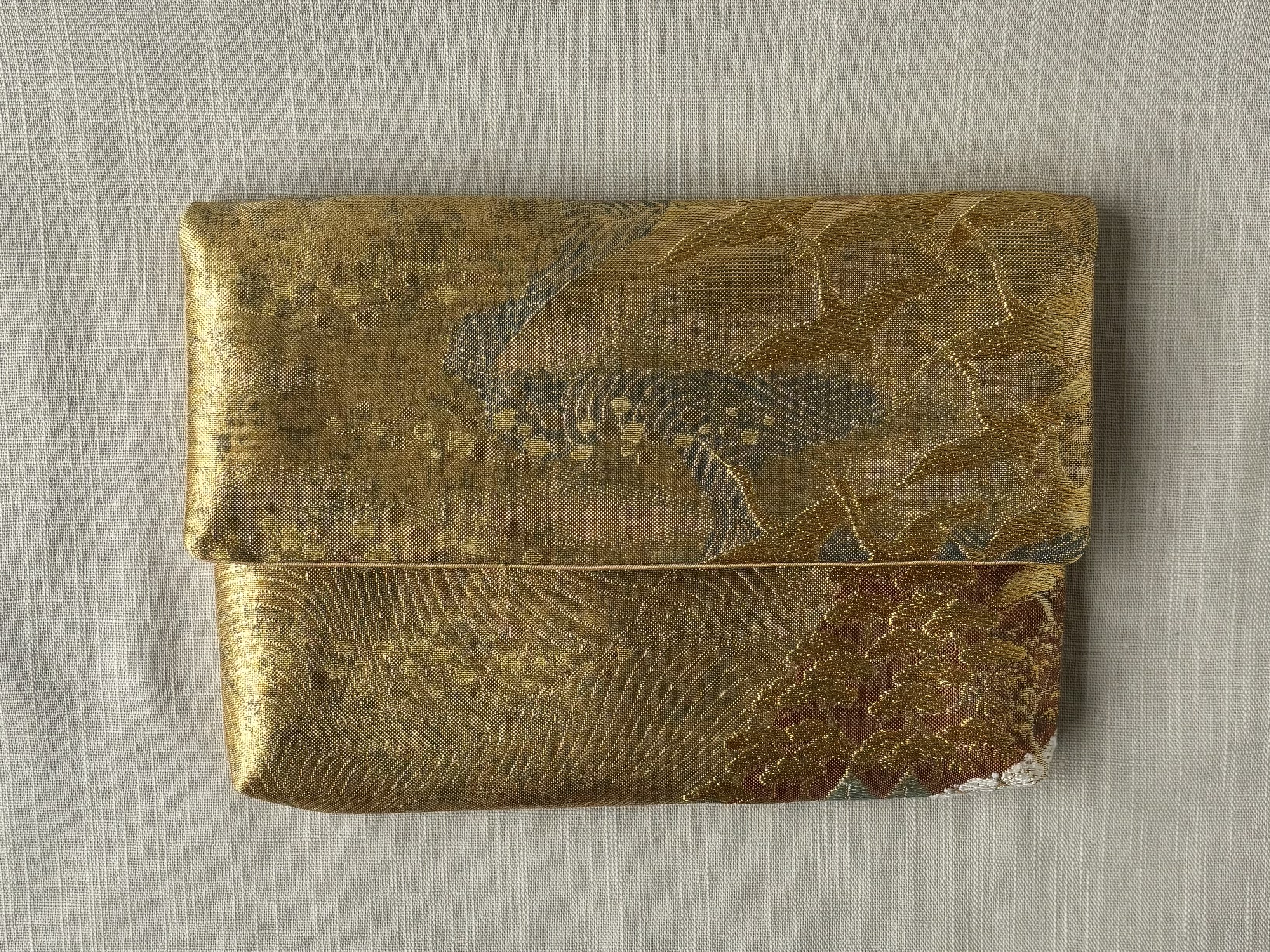 Front view of the clutch without chain on cream coloured textured linen background, showing a group of cranes flying across a backdrop of mountains and rust coloured wood.