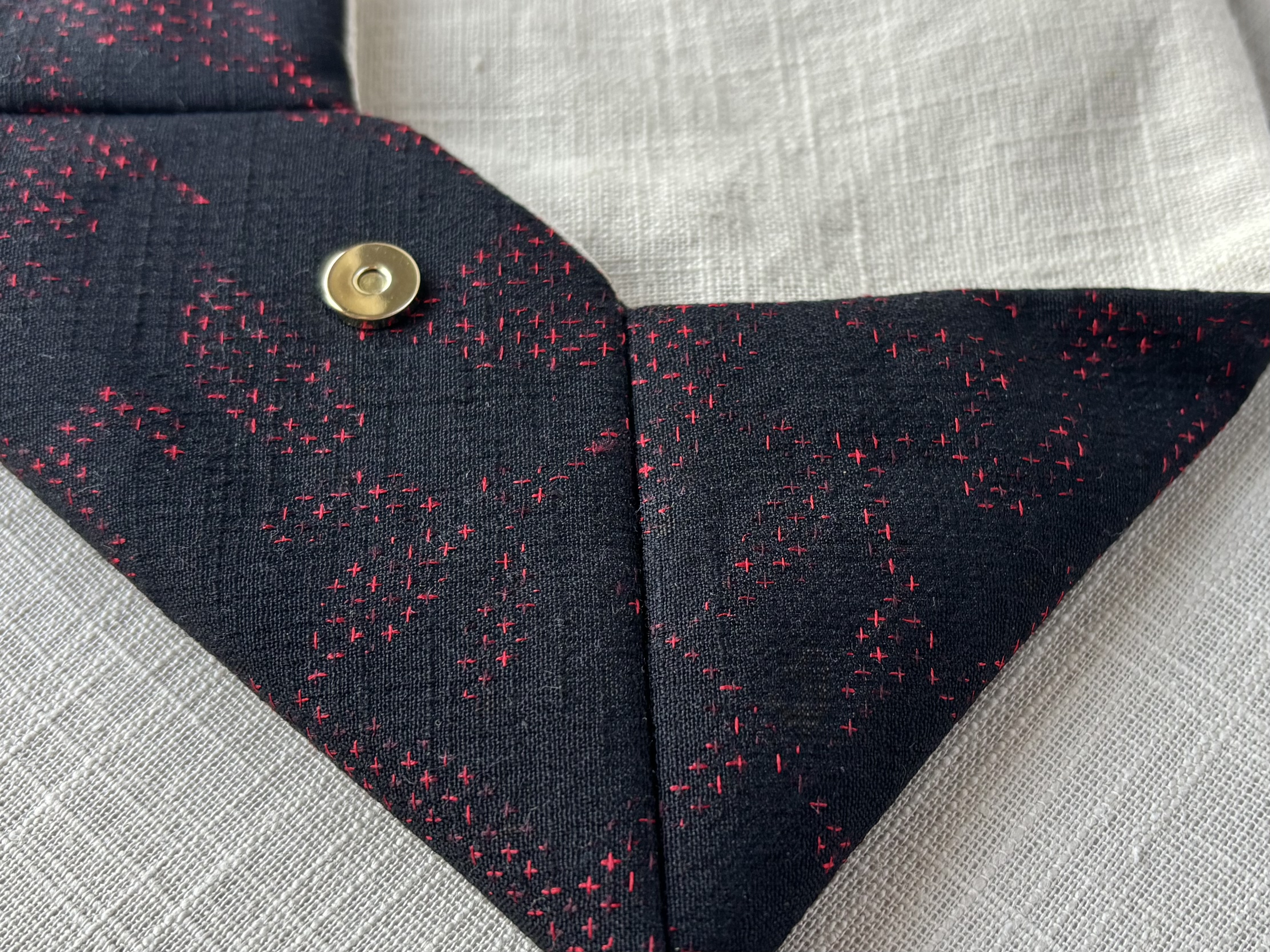 Close up of the side of the sukiya bag showing the structure of the black wool and red cross stitch pattern, as well as brass magnetic closure.